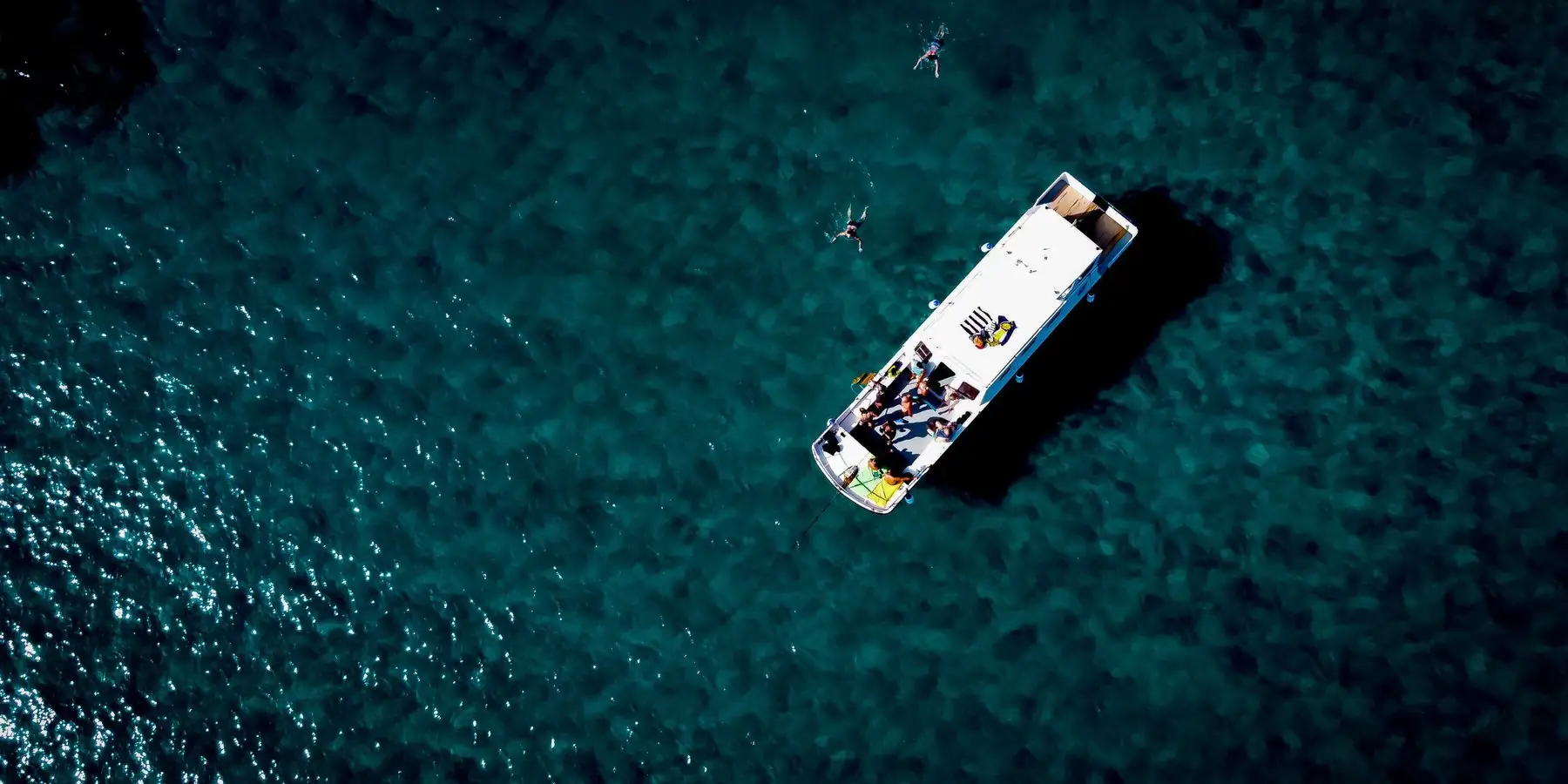 Una lancha vista desde el aire sobre el mar azul, con gente en el agua