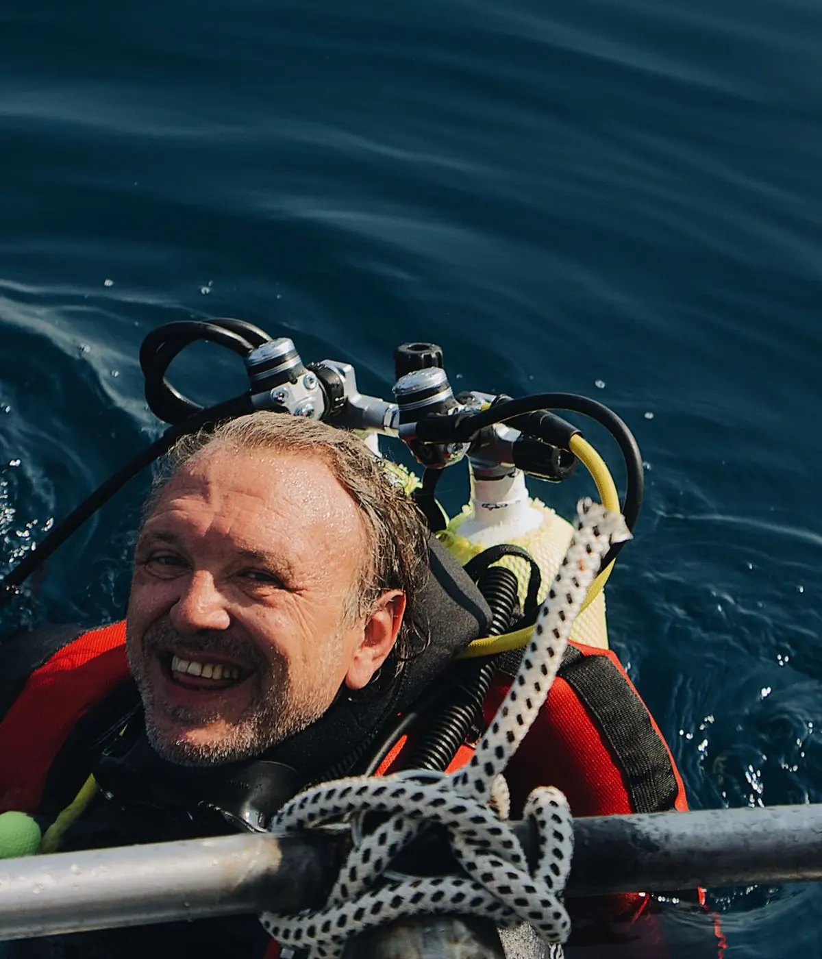 Un buzo sale del agua sonriendo, agarrado de la escalera de la lancha